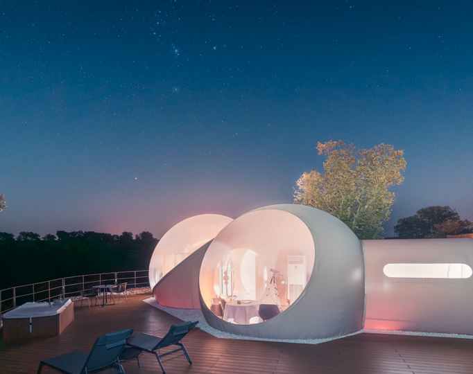Hotel Miluna iluminado por la noche bajo un cielo estrellado, con terraza de madera, jacuzzi y tumbonas rodeadas de naturaleza