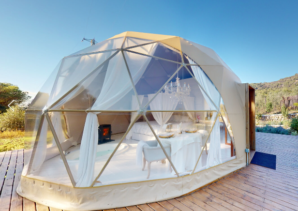 Cúpula geodésica de lujo en plena naturaleza con decoración blanca elegante, mesa de comedor y cama con dosel, iluminada por la luz del día
