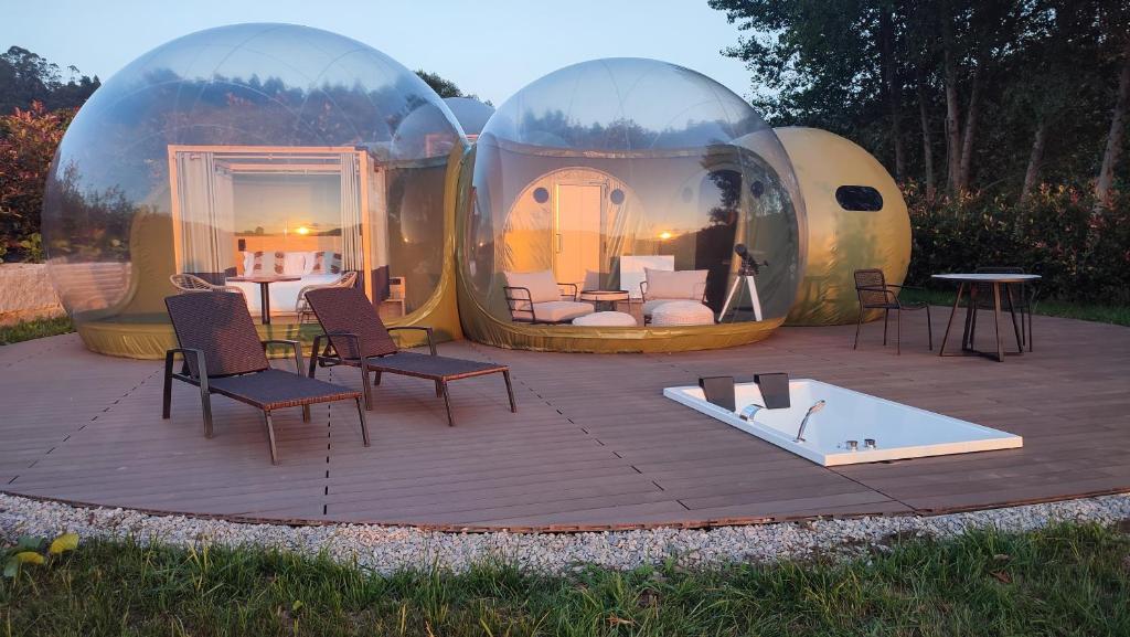Burbuja doble transparente con zona de estar y dormitorio, terraza equipada con tumbonas, jacuzzi exterior y vistas al atardecer en un entorno natural
