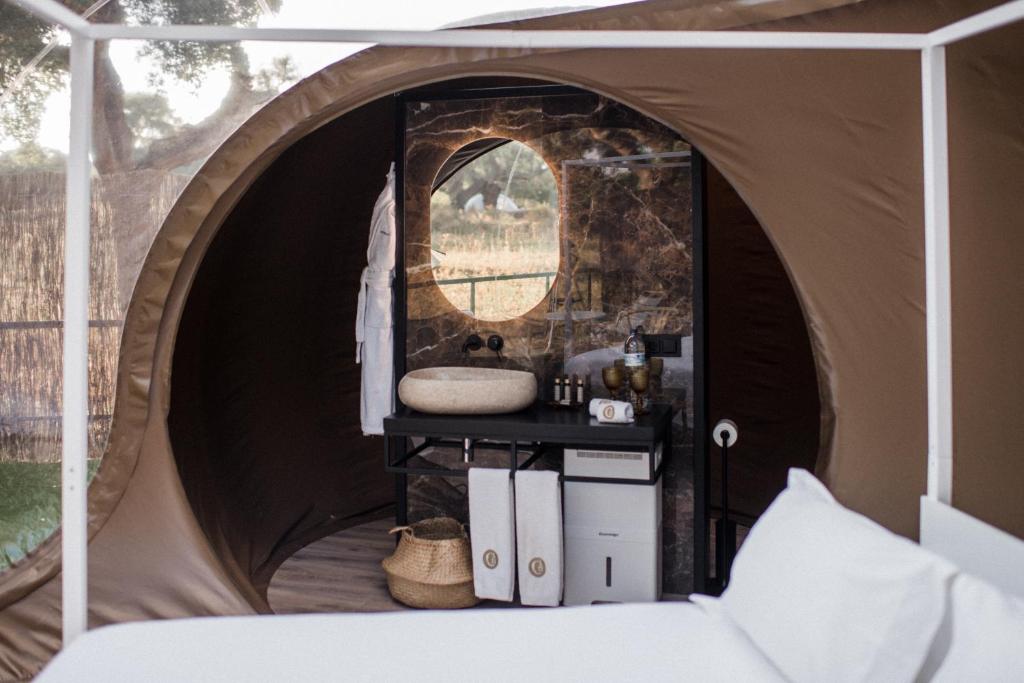 Baño de diseño dentro de una burbuja glamping, con lavamanos de piedra sobre encimera negra, espejo circular y detalles