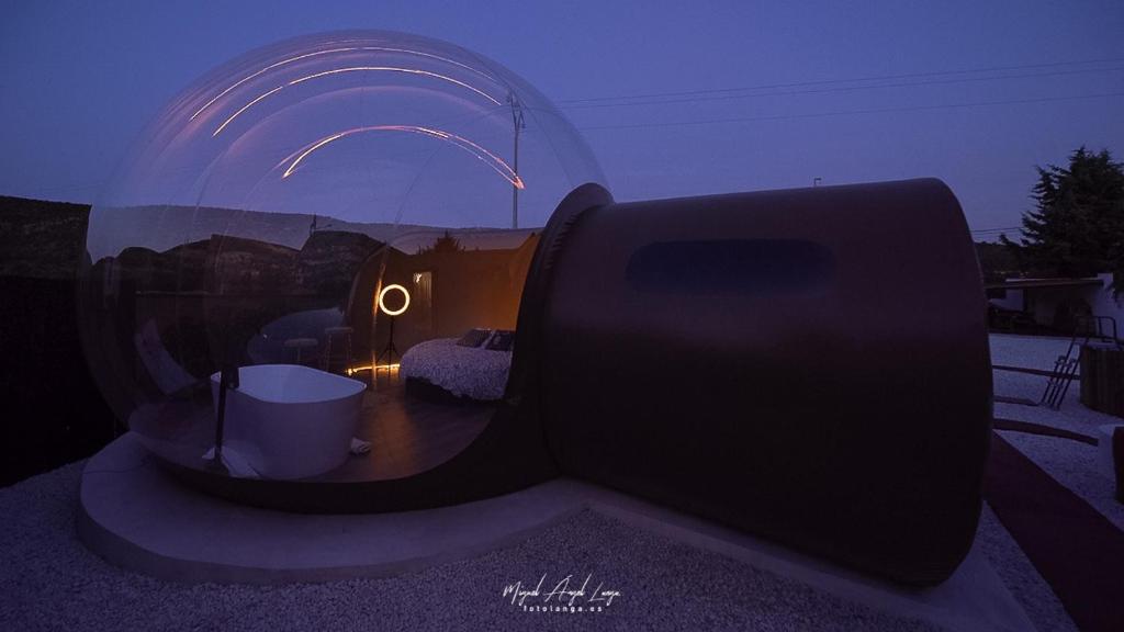 Hotel Burbuja transparente con bañera exterior y cama doble, iluminada con luz ambiental cálida durante el atardecer, en un entorno íntimo y moderno