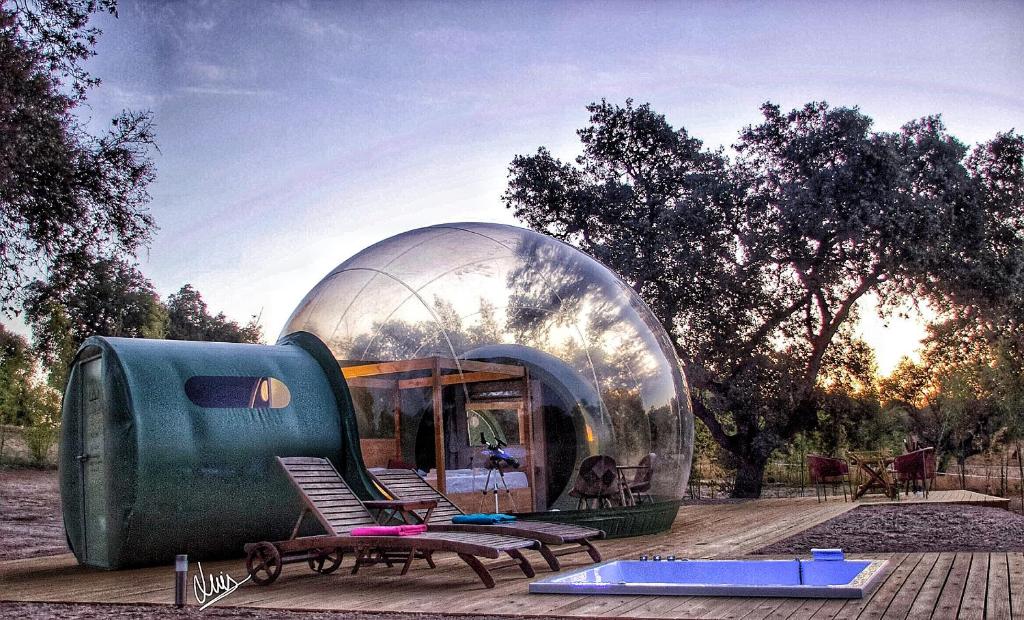 Burbuja transparente en medio del bosque con terraza de madera, tumbonas, piscina pequeña y mobiliario de exterior, ideal para una escapada en la naturaleza