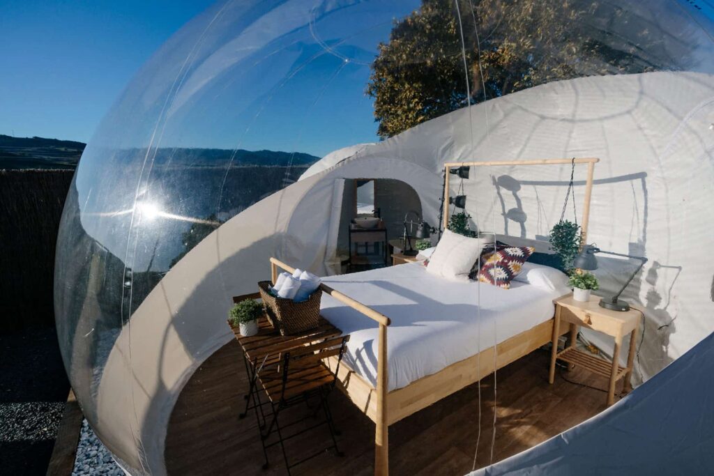 Burbuja de glamping transparente con cama doble, decoración acogedora y vistas a la naturaleza