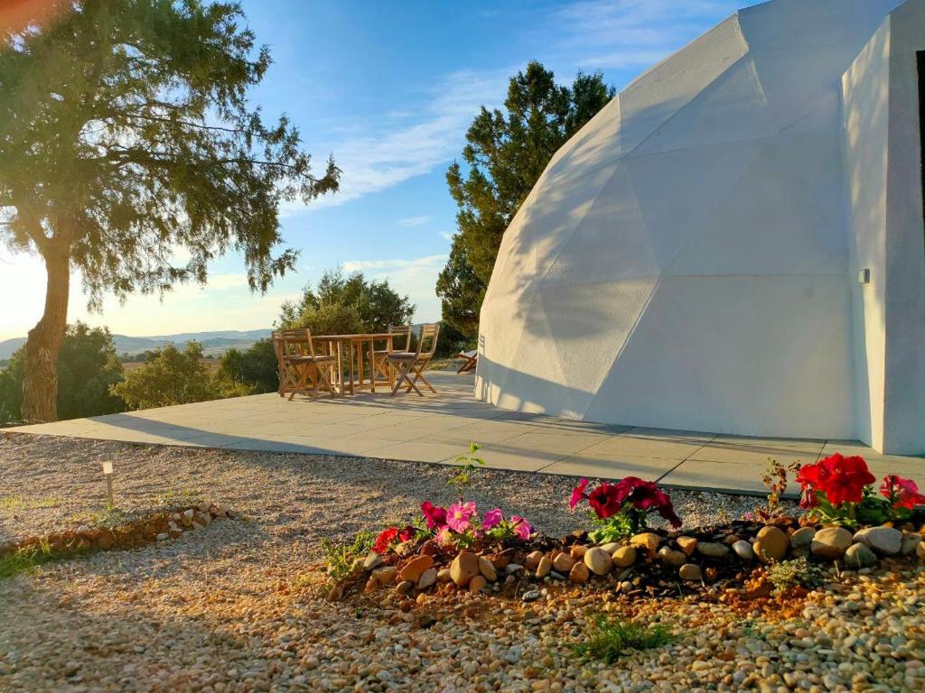 Domo geodésico blanco con terraza exterior, mesa de madera, flores en primer plano y vistas a las montañas al atardecer