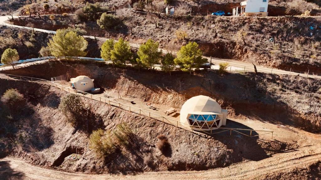 Vista aérea de domos geodésicos para glamping ubicados en una colina, rodeados de naturaleza y caminos rurales