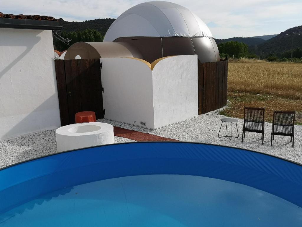 Zona exterior de hotel burbuja con piscina desmontable, sillas, mesa auxiliar y paisaje de campo al fondo