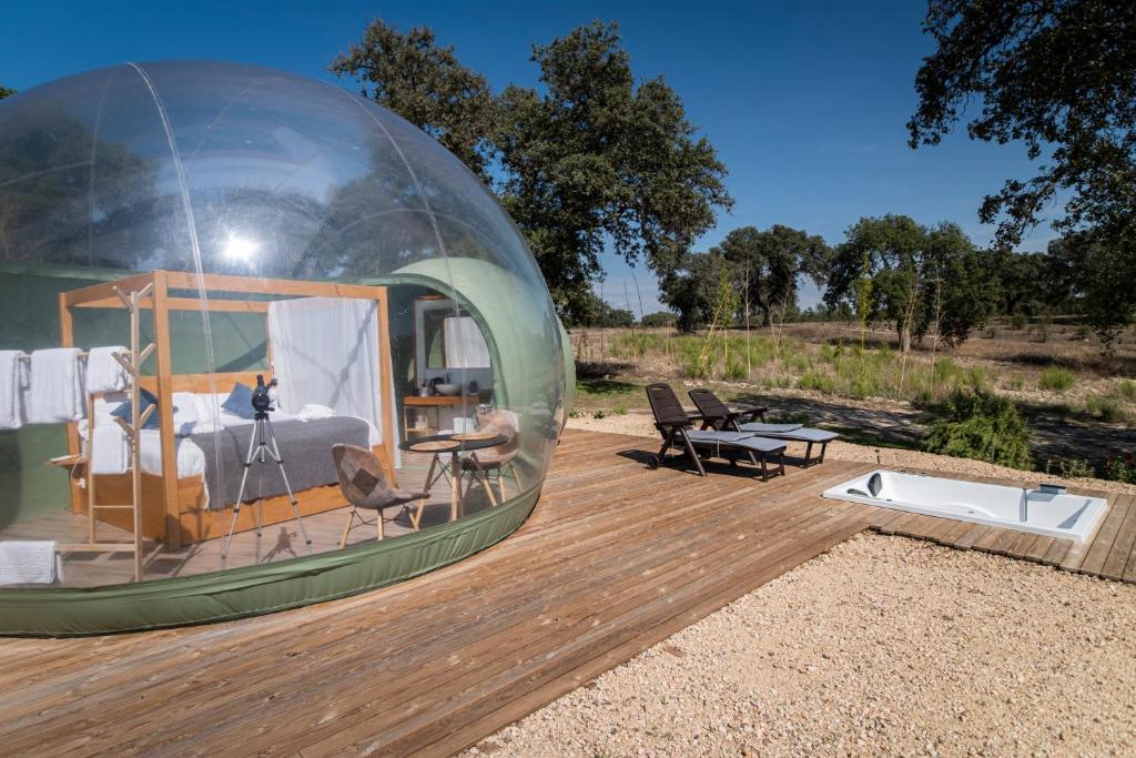 Hotel burbuja con cama con dosel, telescopio, terraza de madera, tumbonas y jacuzzi exterior rodeado de naturaleza en un día soleado