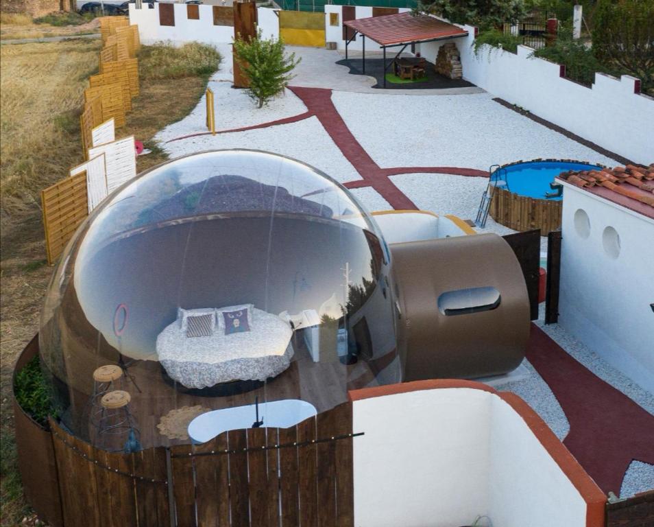 Vista aérea de hotel burbuja con cama redonda, terraza privada con taburetes y zona exterior con piscina y espacio común