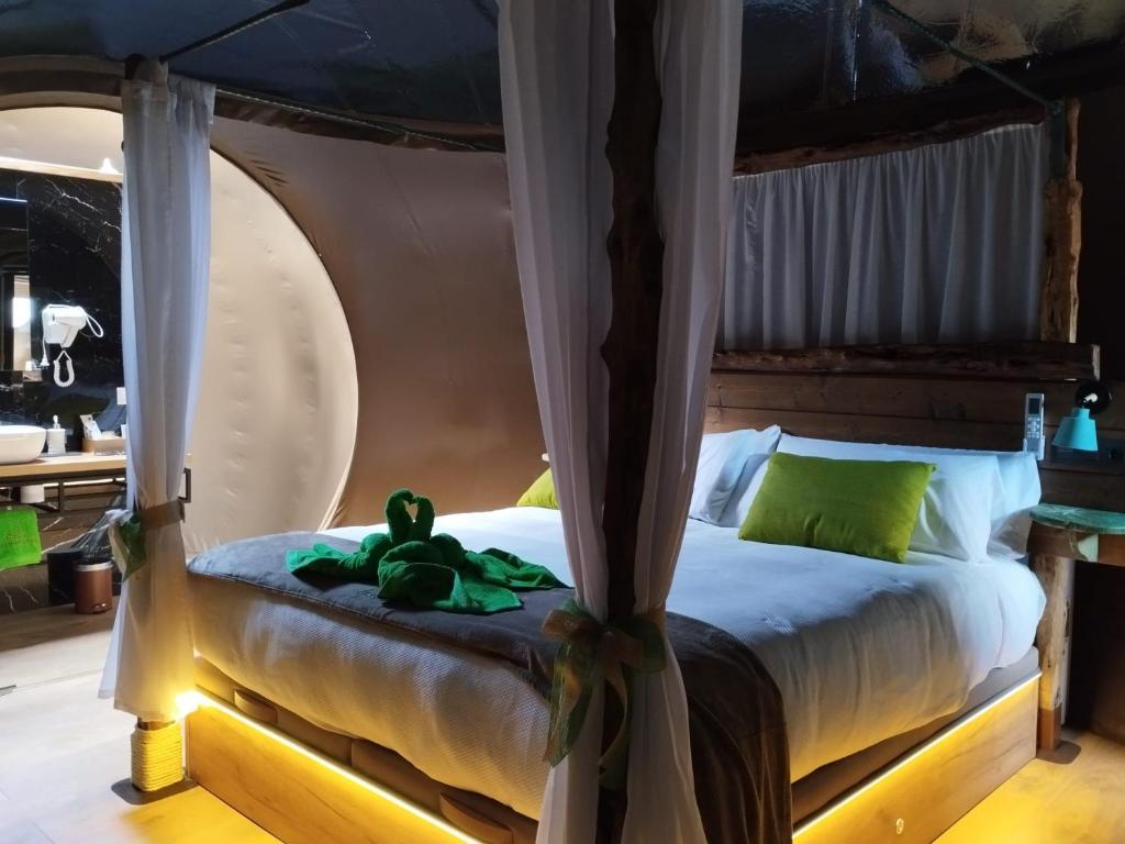 Interior de una burbuja con cama con dosel de madera, iluminación cálida, decoración rústica y acceso a baño moderno visible al fondo