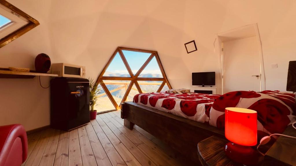Interior de una cúpula glamping con cama doble, ventana triangular con vista a las montañas, y mobiliario moderno