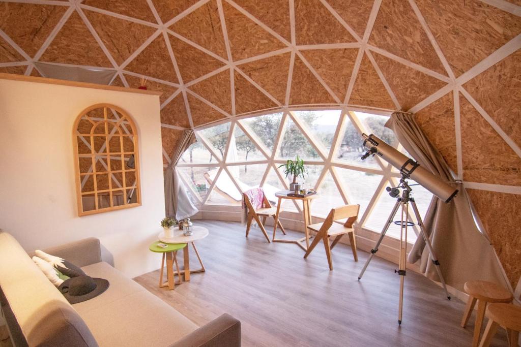 Interior de domo geodésico con sofá, mesa, sillas de madera, telescopio y ventanales con vistas al paisaje natural