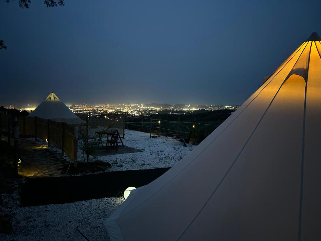 Tiendas de glamping iluminadas por la noche con vista panorámica de la ciudad al fondo