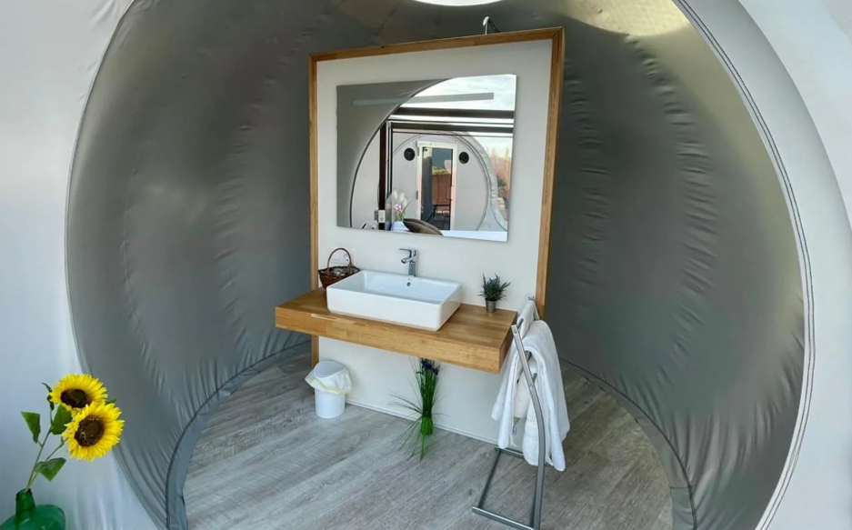 Baño de glamping con lavabo moderno, espejo grande, decoración minimalista y detalles naturales como girasoles y plantas