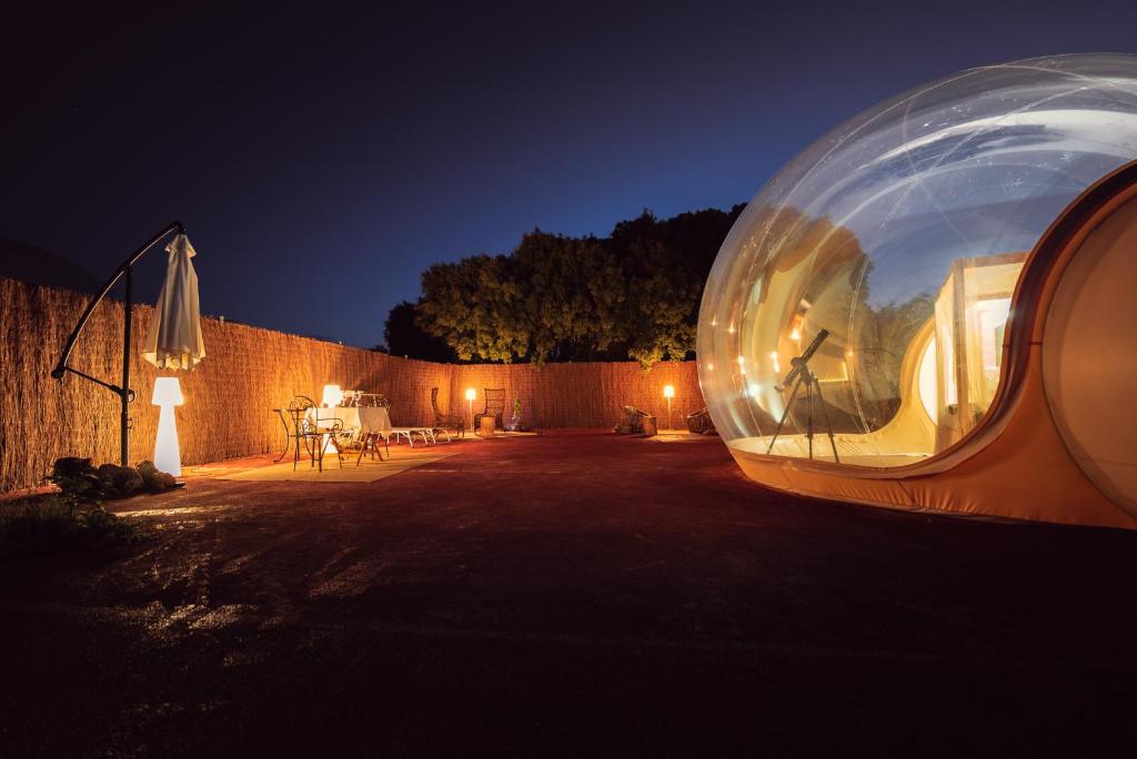 Burbuja de hotel iluminada por la noche con telescopio, terraza privada, mesa con sillas y lámparas ambientales