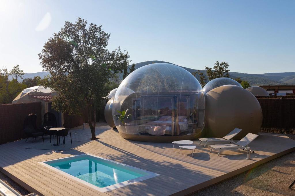 Burbuja de hotel con terraza privada, piscina, tumbonas y mobiliario de exterior, rodeada de montañas y vegetación