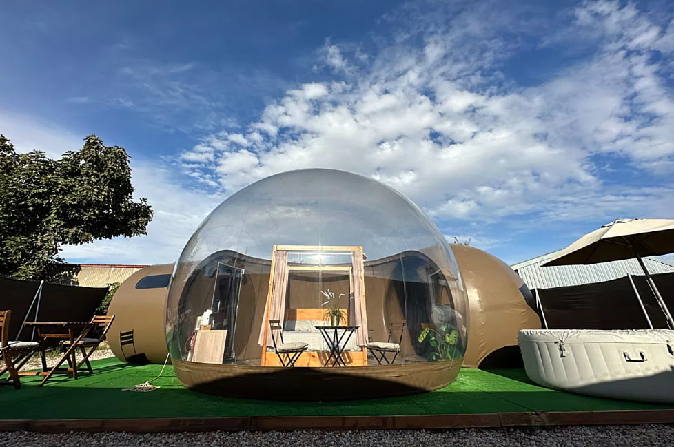 Burbuja transparente con cama doble, jacuzzi exterior y mobiliario de jardín en alojamiento glamping en Alicante