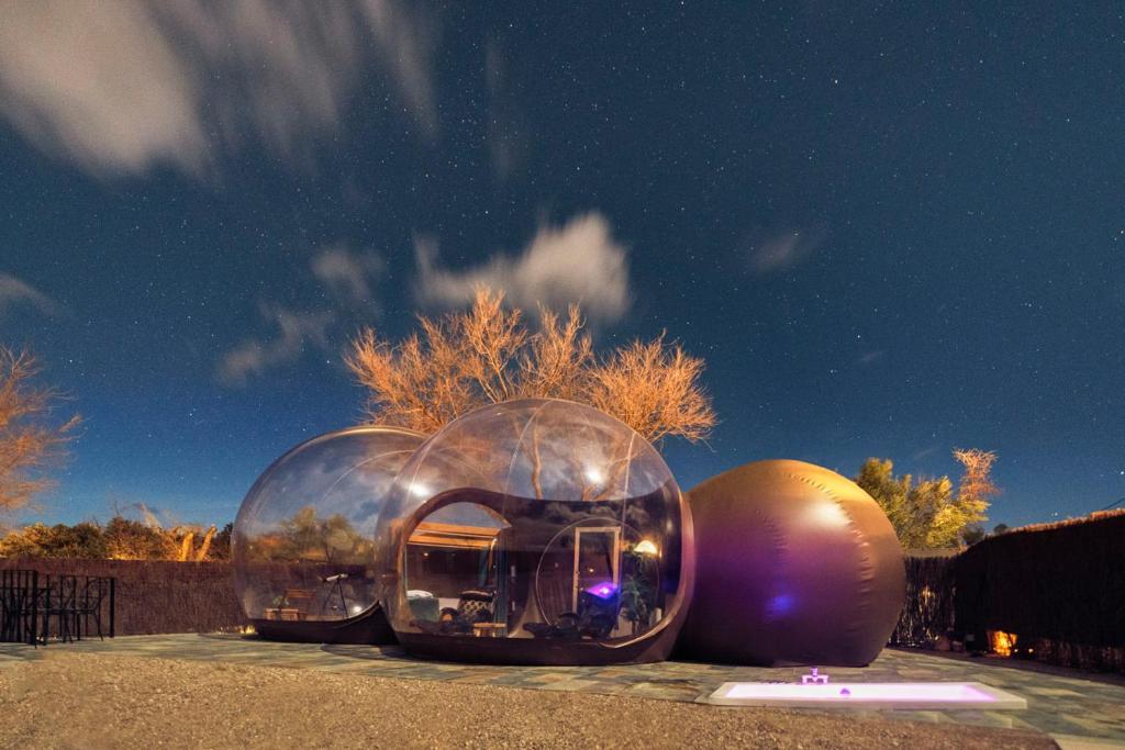Burbuja transparente iluminada bajo un cielo estrellado, con jacuzzi exterior y entorno natural ideal para una escapada romántica nocturna