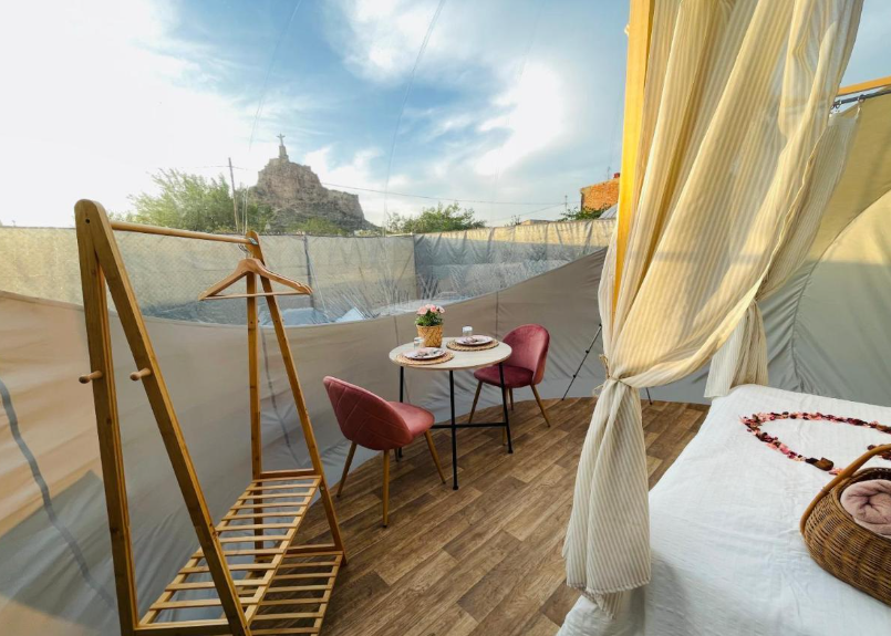Interior de burbuja con mesa para dos, cama con dosel y vistas al castillo de Monteagudo desde la ventana transparente