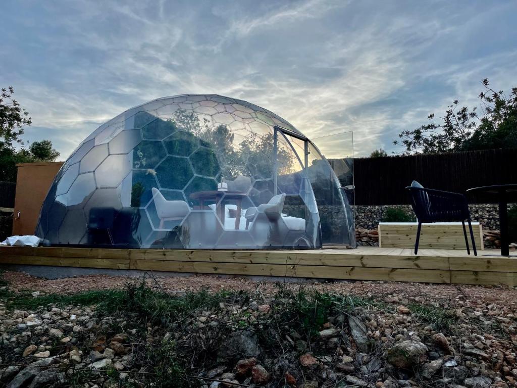 Domo transparente con estructura hexagonal, terraza de madera y mobiliario moderno en un entorno natural