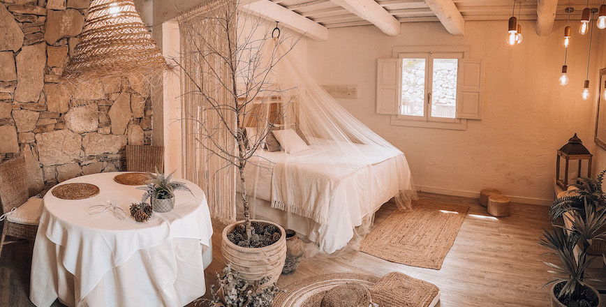Habitación rústica decorada en tonos cálidos con cama con dosel, paredes de piedra y detalles naturales en madera y mimbre.
