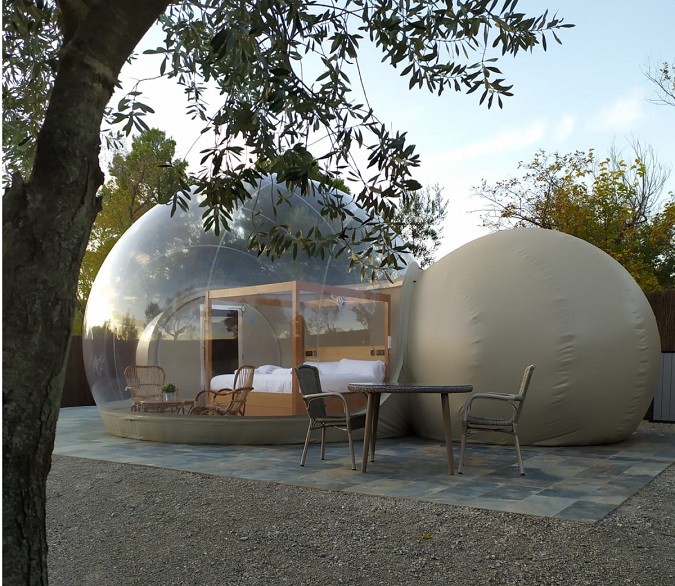 Cúpula transparente de hotel burbuja con cama doble y mobiliario exterior sobre plataforma pavimentada