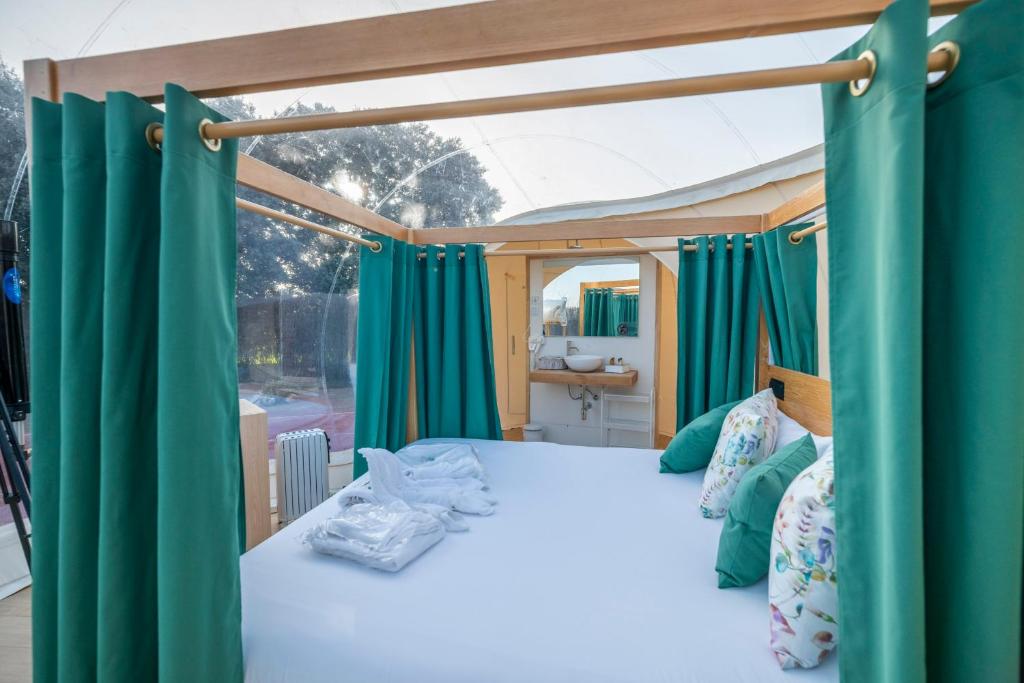 Interior de burbuja de hotel con cama doble, cortinas verdes, cojines decorativos y lavabo con espejo al fondo