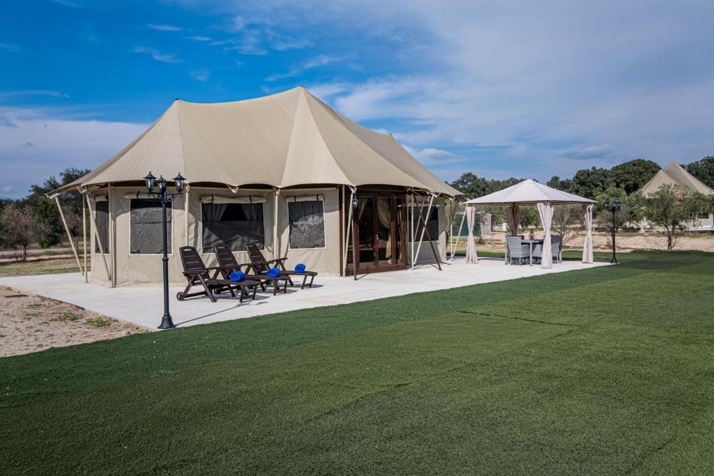 Tienda de glamping de lujo con tumbonas, comedor exterior cubierto y amplio jardín con césped artificial