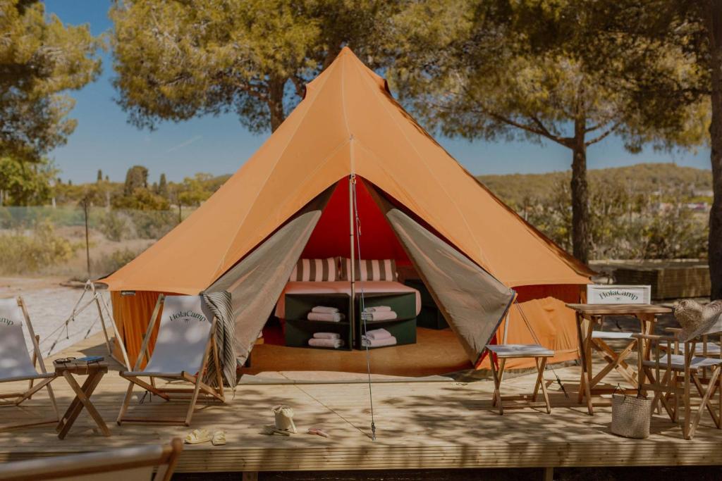 Tienda de glamping color naranja con cama interior, sillas y mesas de madera al aire libre en un entorno boscoso