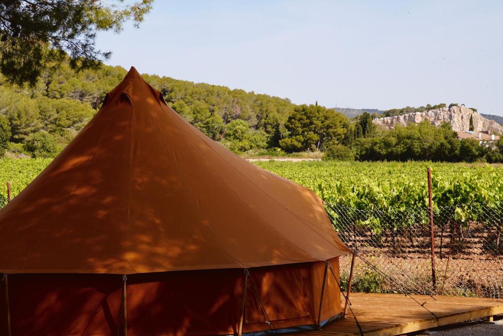 Tienda de glamping color naranja junto a un viñedo, rodeada de naturaleza y montañas al fondo