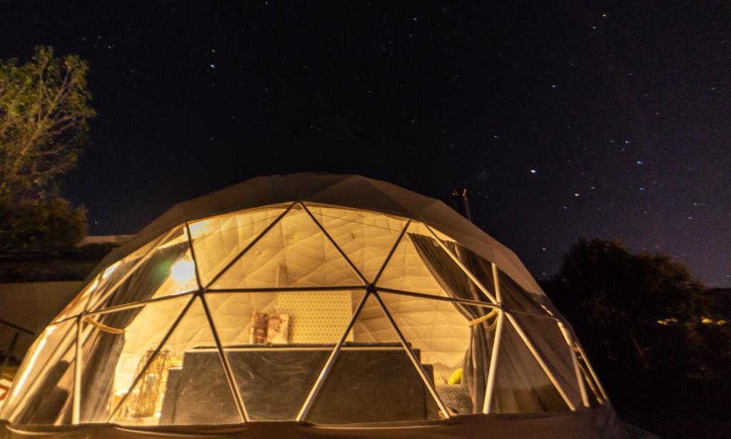 Domo geodésico iluminado desde el interior, con grandes ventanales y vista del cielo estrellado en la noche
