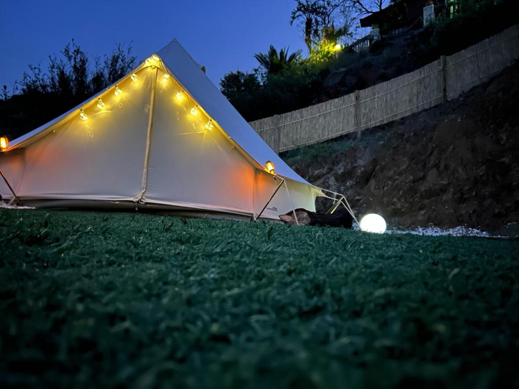 Tienda tipo tipi iluminada con luces decorativas por la noche, en un entorno natural con césped y colina al fondo