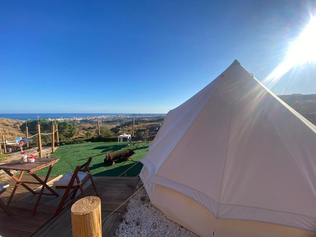Tienda tipo tipi en zona de glamping con terraza de madera y vistas panorámicas al mar y la ciudad a lo lejos